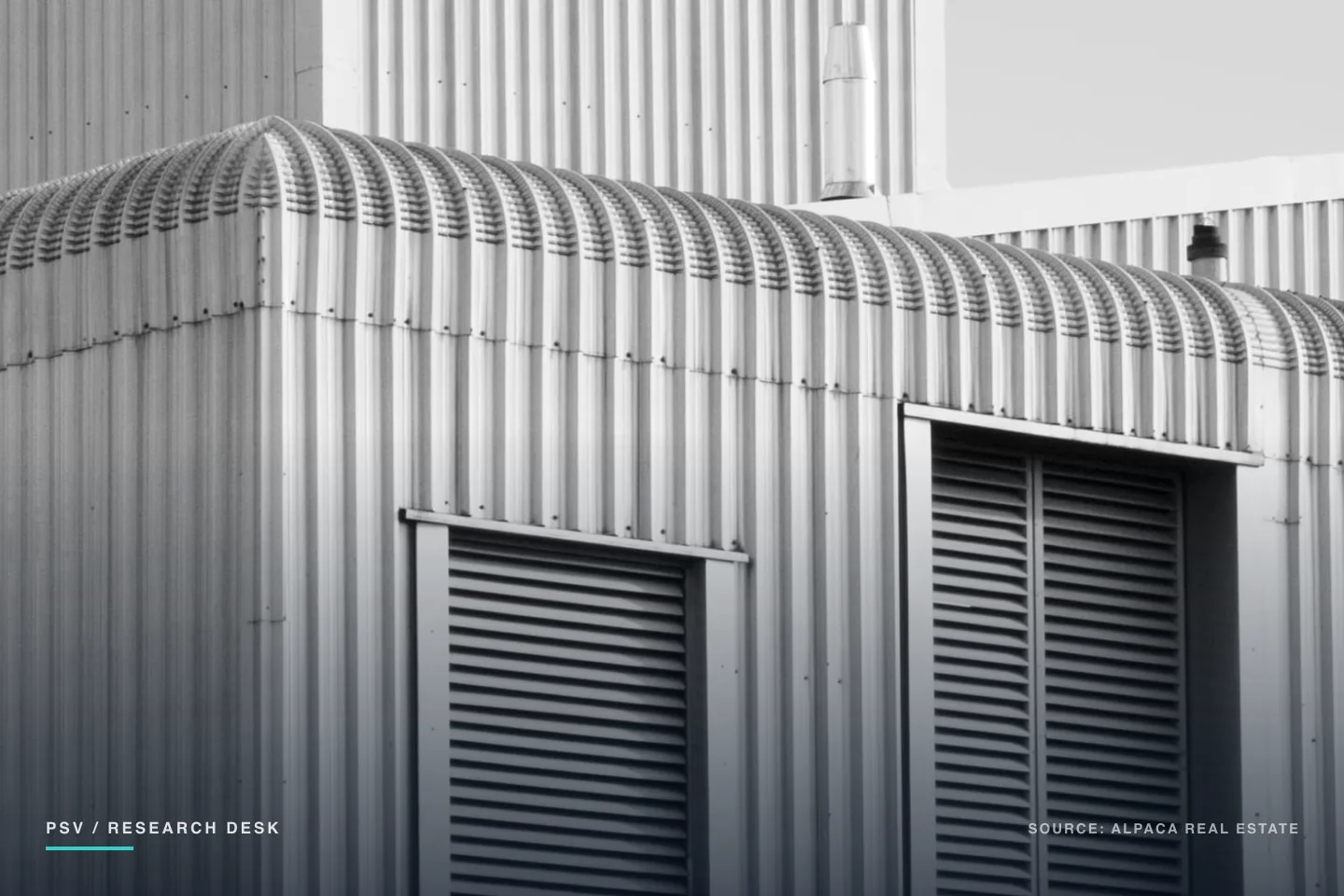 Black and white photograph of a single-story industrial building shot from below against a bright sky, its walls and barrel-vaulted roof clad in vertical corrugated metal, with two tall louvred vents set into the near elevation and a metal flue rising from a taller structure behind it Black and white photograph of a single-story industrial building shot from below against a bright sky, its walls and barrel-vaulted roof clad in vertical corrugated metal, with two tall louvred vents set into the near elevation and a metal flue rising from a taller structure behind it