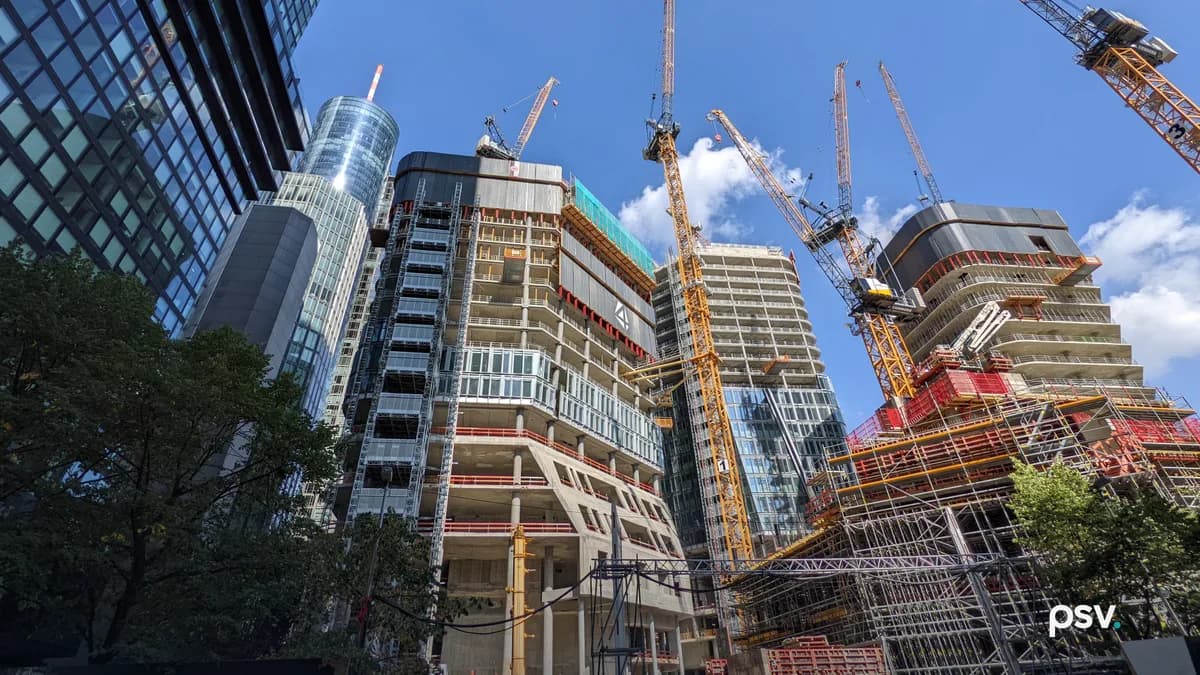 Looking up from street level at several high-rise towers under construction in Frankfurt's financial district: exposed concrete slabs and columns, climbing formwork, safety screens, partly installed glass curtain wall, and tower cranes against a blue sky.