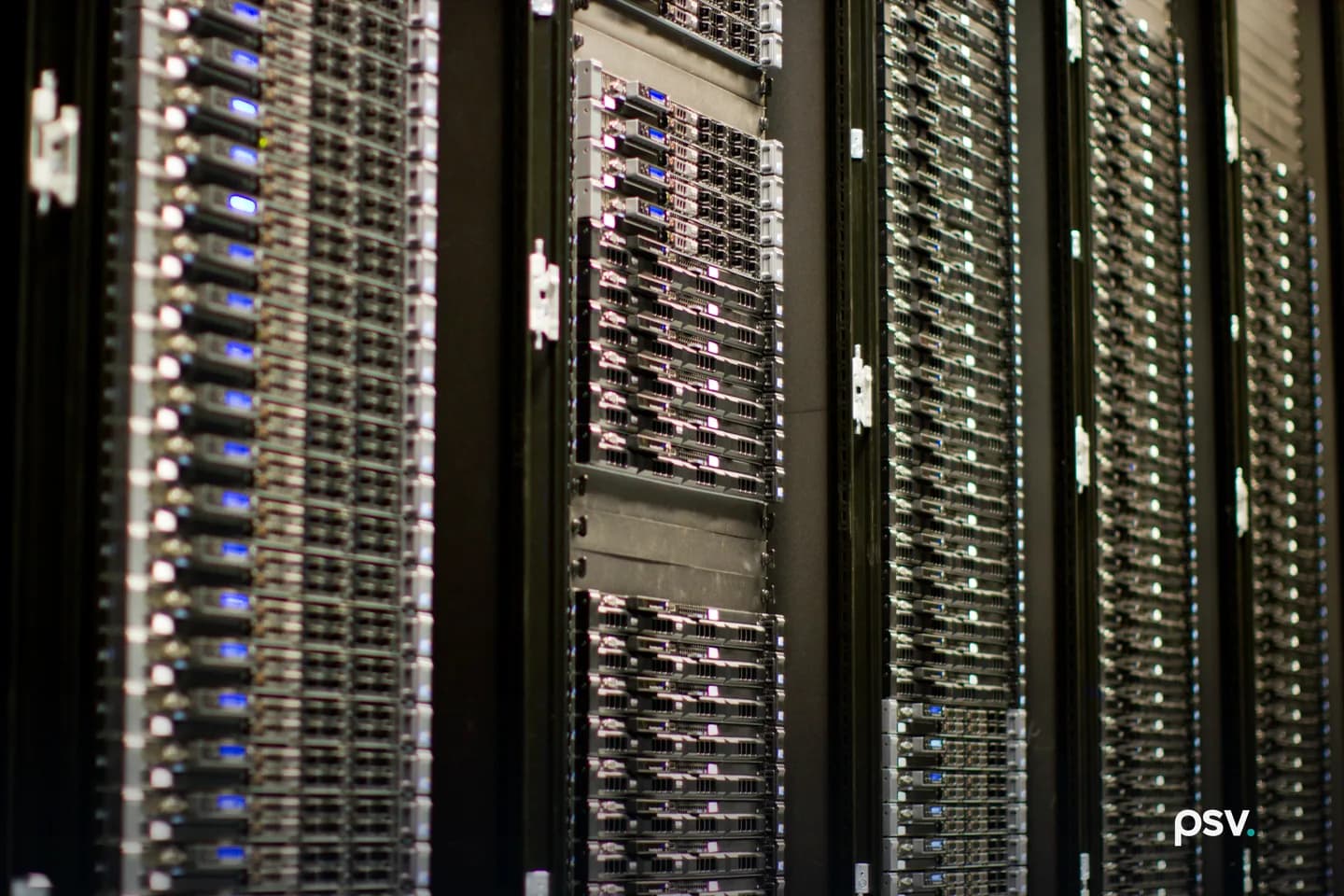Close view of four black equipment racks packed with rows of rack-mounted servers, their front panels showing drive bays and small blue and white status lights, receding at an angle into shadow.