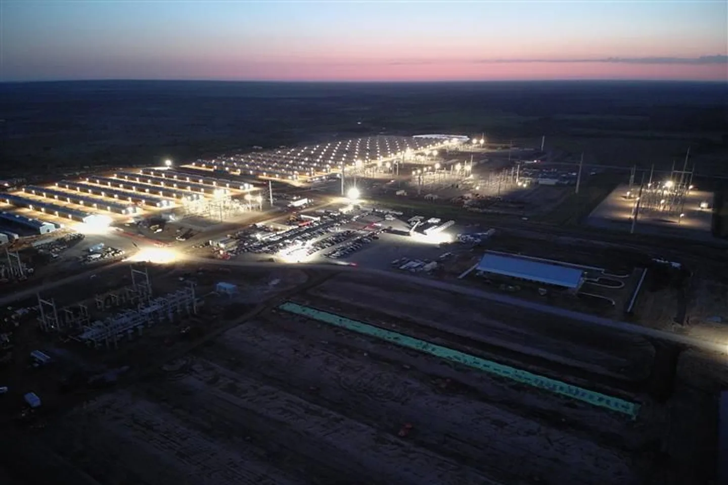 Aerial night view of IREN’s Childress, Texas data center campus: rows of illuminated data halls, on-site electrical substations, and graded expansion pads under a dusk sky Aerial night view of IREN’s Childress, Texas data center campus: rows of illuminated data halls, on-site electrical substations, and graded expansion pads under a dusk sky